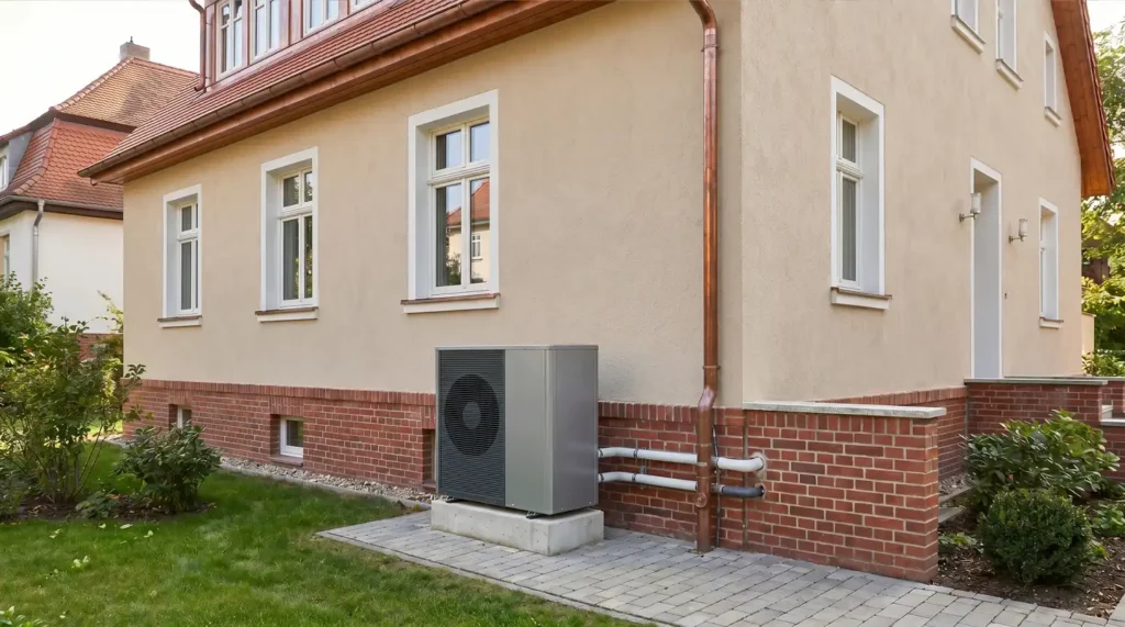 Luft-Wasser-Wärmepumpe vor einem gepflegten Altbau mit Klinkersockel und klassischen Fenstern.